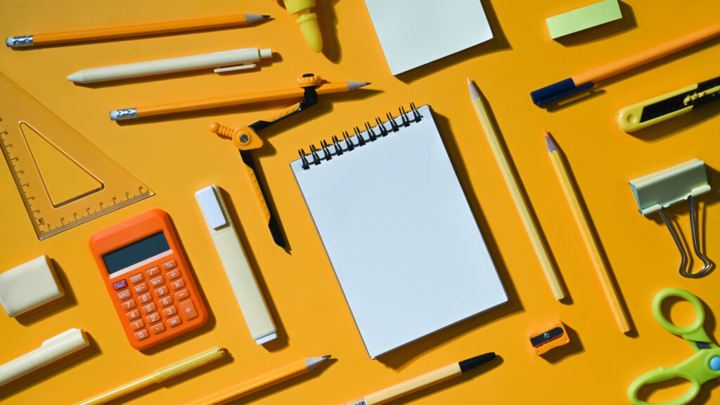 Blank notepad and various school supplies on yellow background.